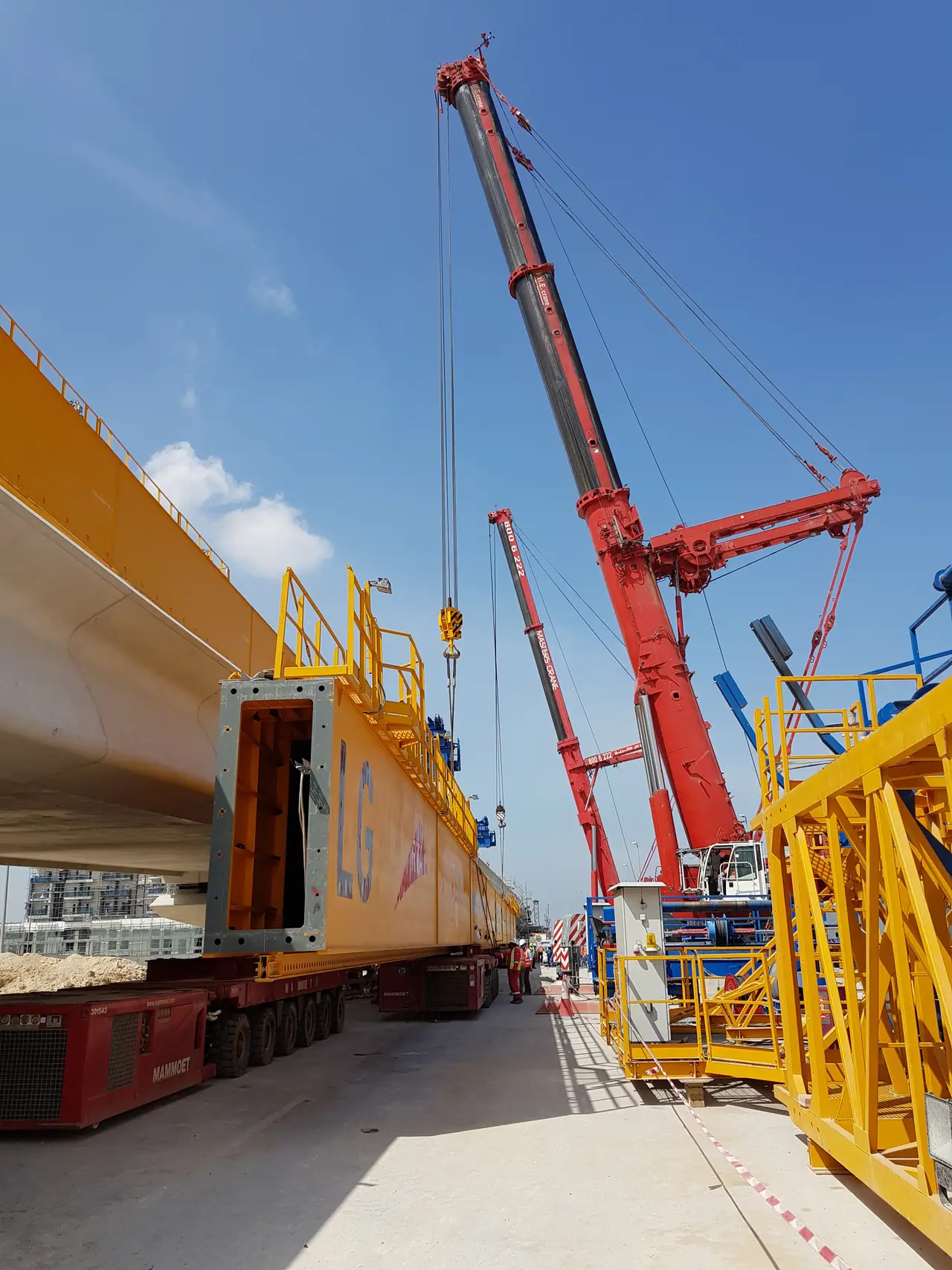 Red mobile crane beside a bridge box-girder segment loaded on a multi-axle modular trailer