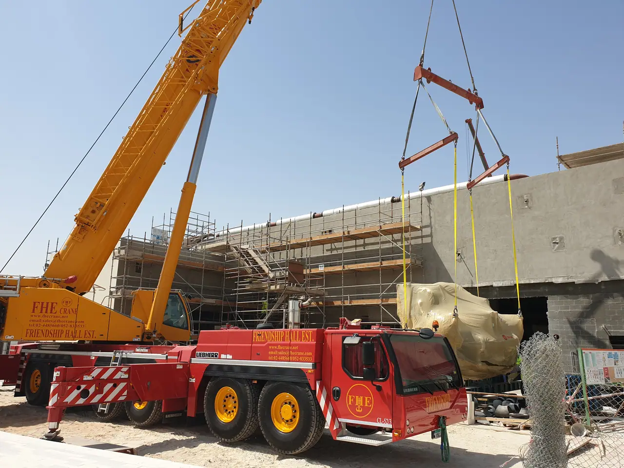 All-terrain crane in Friendship Hall livery lifting wrapped plant equipment into a building