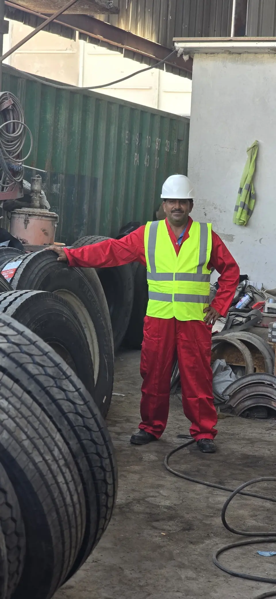 An FHS worker in hard hat, hi-vis vest and coveralls beside stacked heavy-vehicle tyres