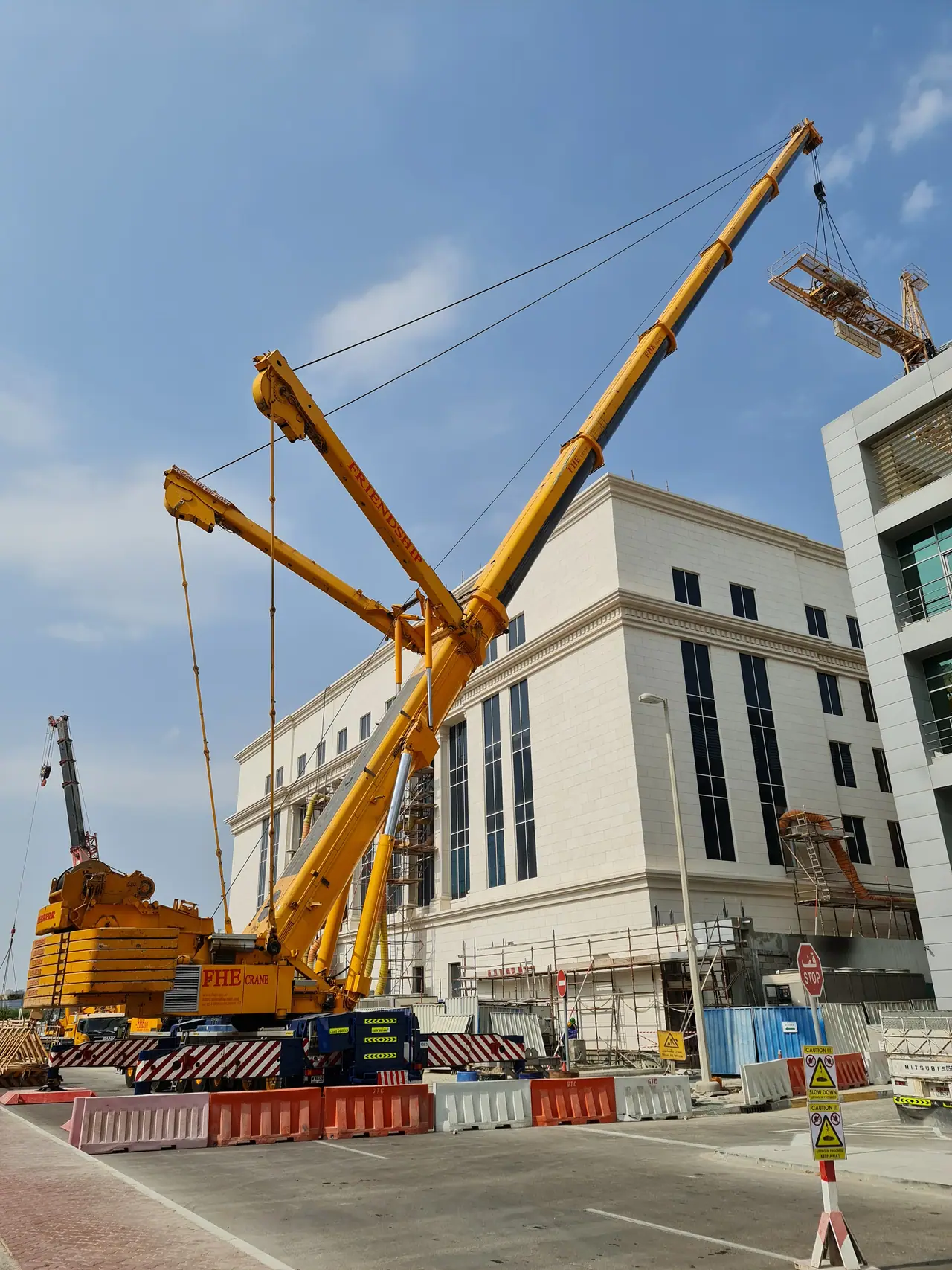 Yellow luffing crane lifting steelwork beside a civic building