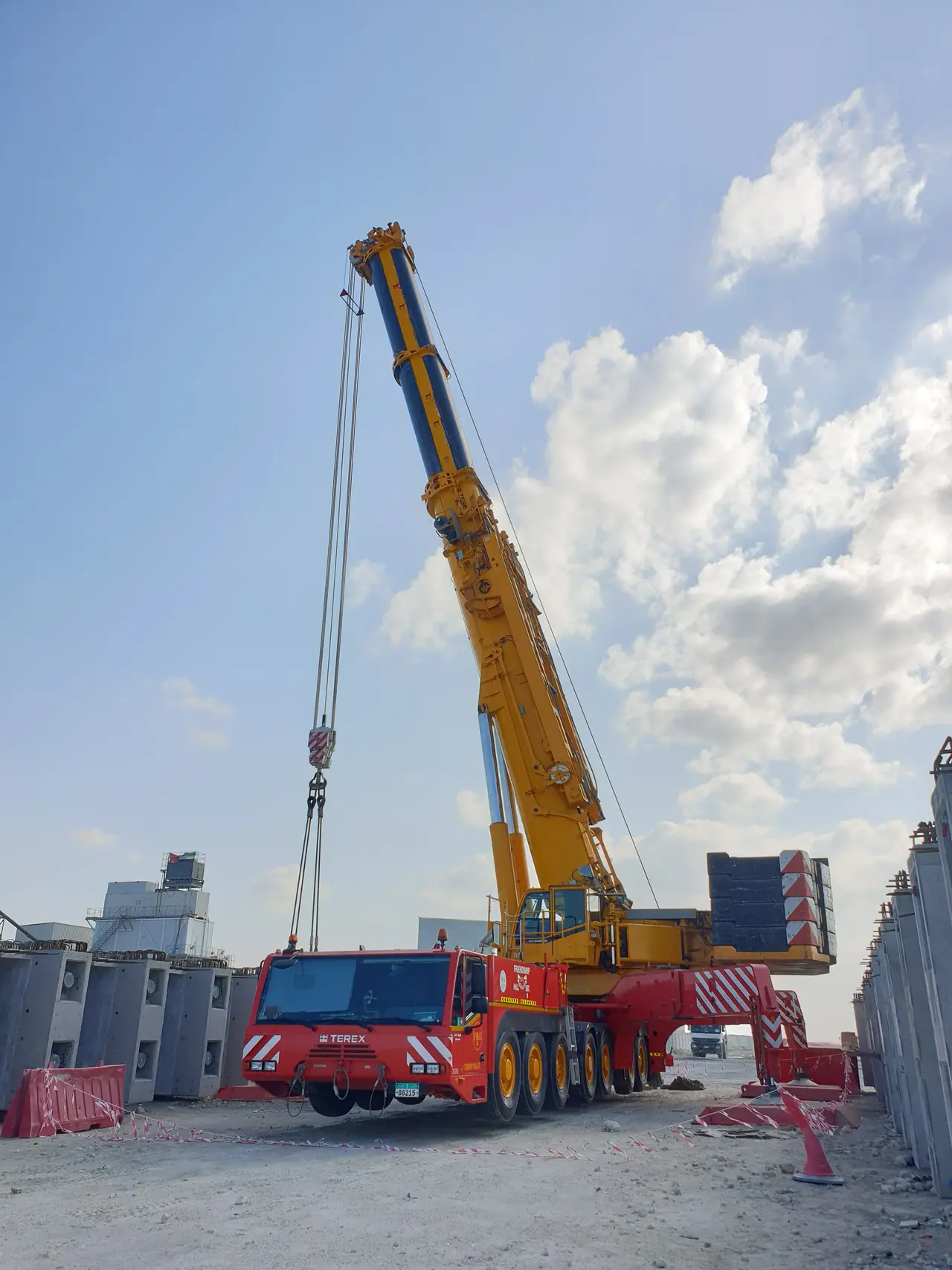 Red and yellow FHE Terex all-terrain crane set up on its outriggers, boom raised