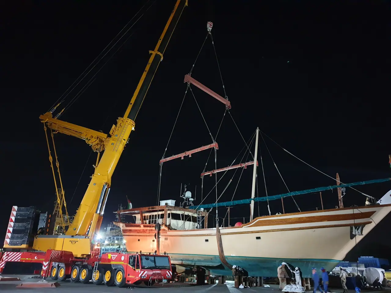 Night lift of a traditional wooden dhow with spreader bars under floodlights