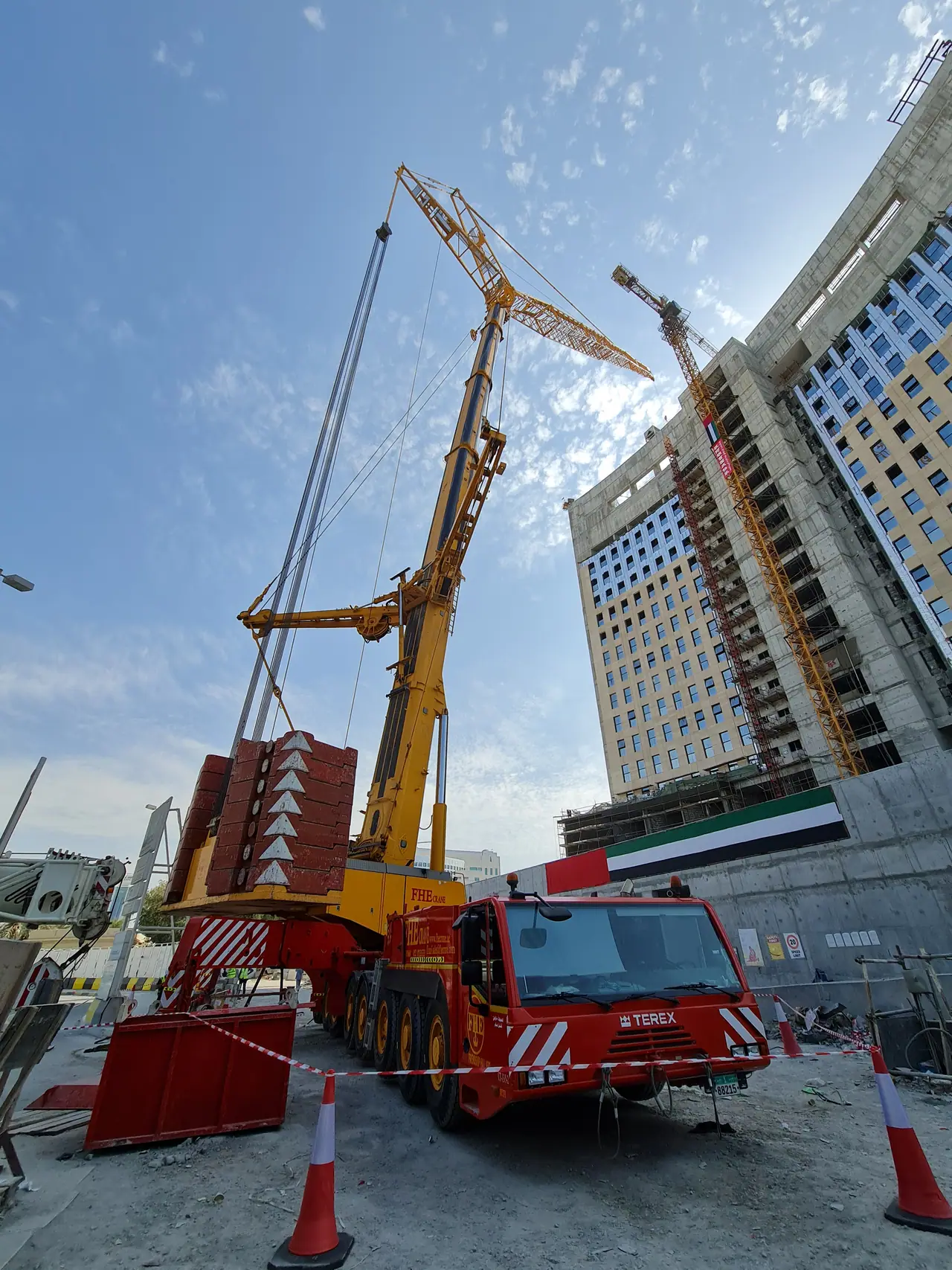 Heavy crane with superlift counterweight beside a tower draped with the UAE flag